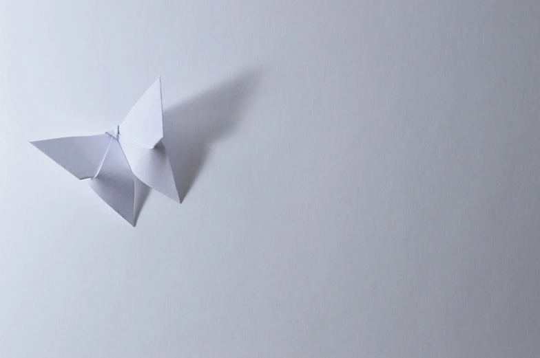 a close up of a paper butterfly on a white surface, unsplash, minimalism, miniature origami figurine, white-space-surrounding, banner, benjamin vnuk