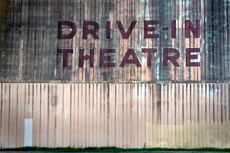 a sign that says drive in theatre on the side of a building, a stock photo, by Dave Melvin, shutterstock, graffiti, rusted panels, 1940s photo, rivers, 90's photo