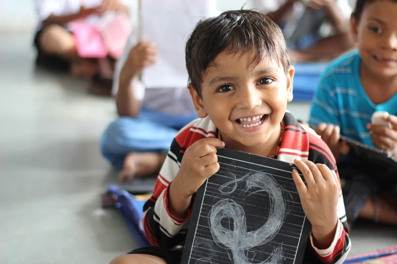 a young boy holding a chalk board with a drawing on it, a picture, bengal school of art, smiling into the camera, teaser, thumbnail, childlike