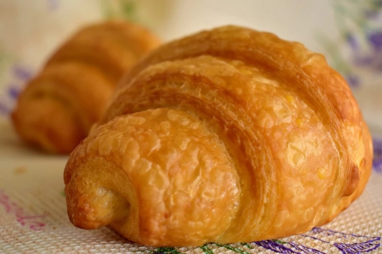 a couple of croissants sitting on top of a table, a portrait, inspired by Károly Patkó, pixabay, photorealism, close up details, paul-chadeisson, with a soft, pastelle