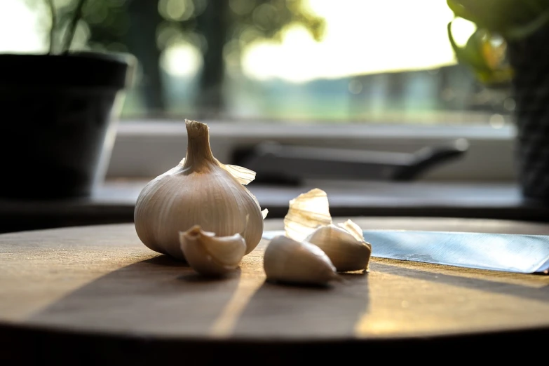 a clove of garlic next to a knife on a table, a macro photograph, pixabay, evening sunlight, vignette of windowsill, 4 k product photo, cracks