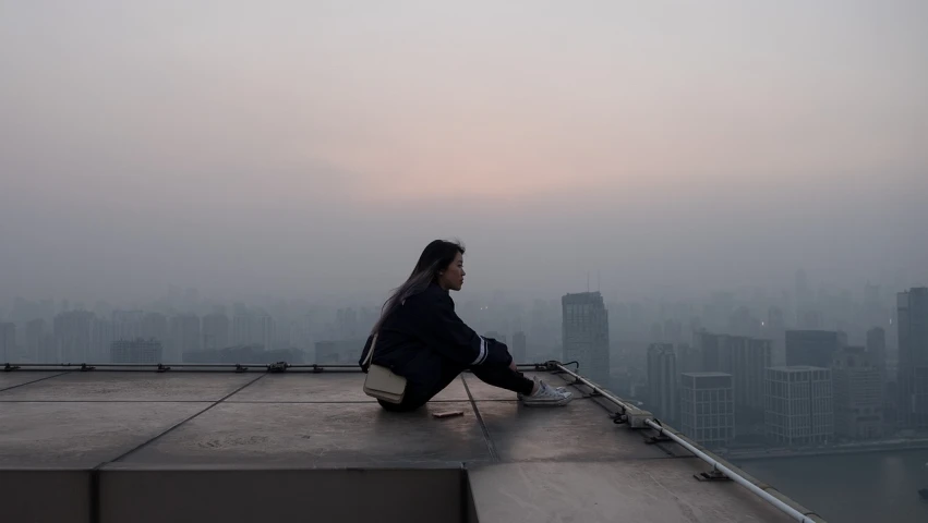 a woman sitting on the edge of a building, inspired by Cheng Jiasui, unsplash contest winner, an ominous haze, end of the day, the sky is gray, young asian girl