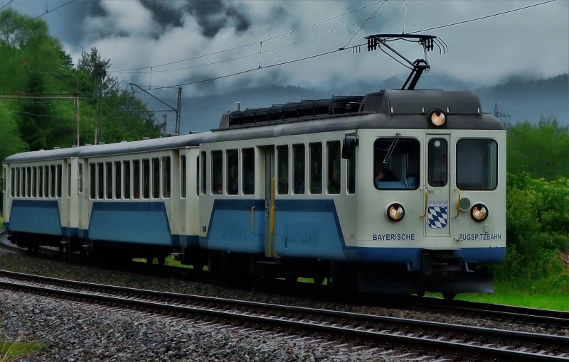 a blue and white train traveling down train tracks, a picture, by Hans Schwarz, flickr, overcast lighting, banner, electric, alpine