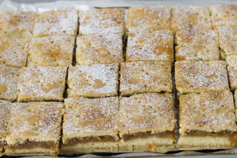 a close up of a tray of food on a table, by Jan Kupecký, apple pie, squares, covered in white flour, closeup photo