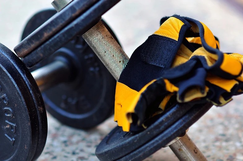 a pair of gloves sitting on top of a pair of dumbs, by Dietmar Damerau, pexels, carrying two barbells, black and yellow colors, cart wheels, foot wraps