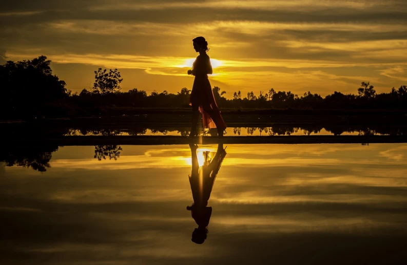 a woman walking across a body of water at sunset, a picture, by Brad Holland, pixabay contest winner, on a reflective gold plate, standing on a lotus, lady using yellow dress, beautiful girl on the horizon