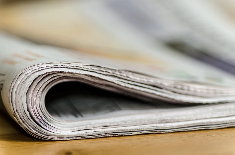 a stack of newspapers sitting on top of a wooden table, a picture, today\'s featured photograph 4k, istock, dynamic closeup, really long