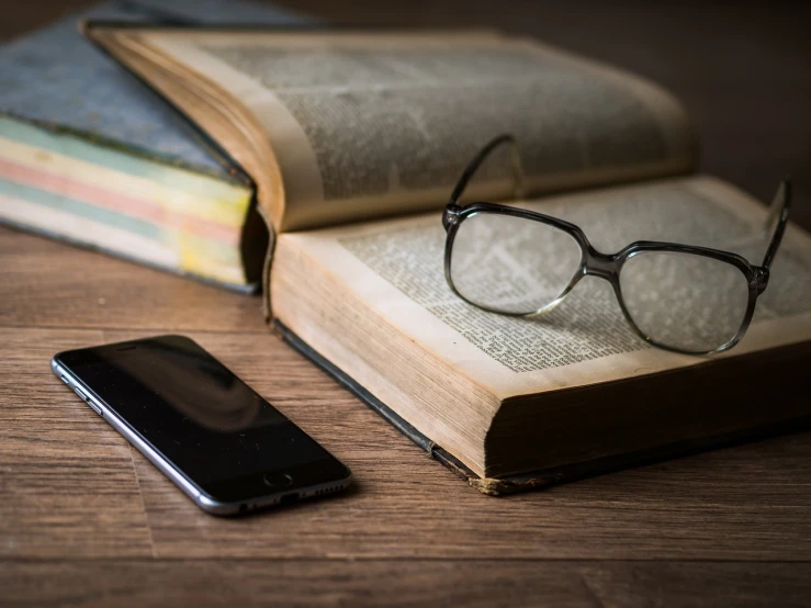a cell phone sitting next to an open book, a portrait, shutterstock, spectacles, old, close - up photo, wood