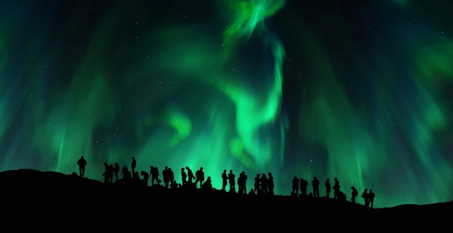 a group of people standing on top of a hill, a picture, by Ejnar Nielsen, shutterstock, northern lights background, crowded silhouettes, set photo, vivid green lasers