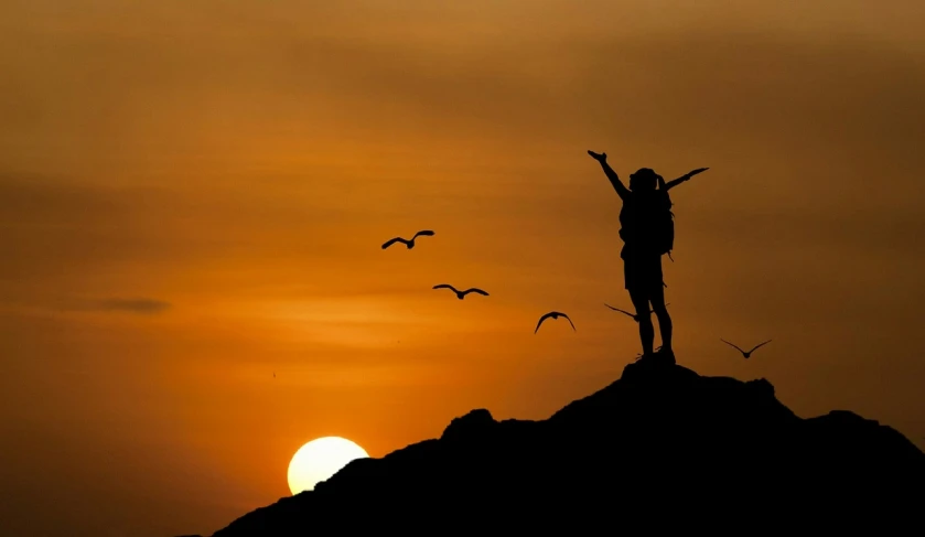 a person standing on top of a mountain at sunset, by Mathias Kollros, pixabay contest winner, figuration libre, avian warrior, hunting, bird on his shoulder, award wining photo