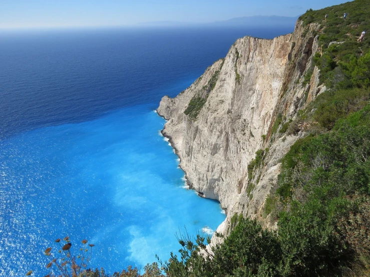 a blue body of water next to a cliff, romanticism, greek nose, eucalyptus, istock, vivid colors!