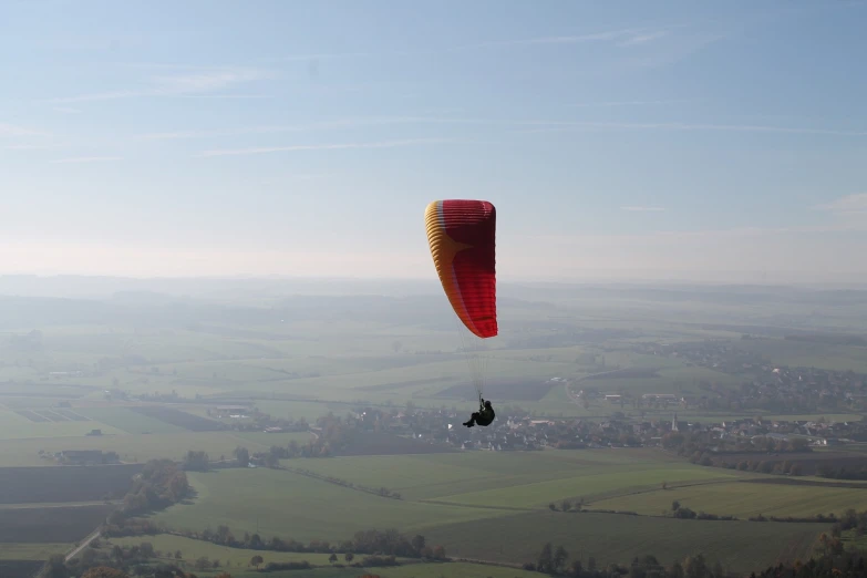 a person that is in the air with a parachute, a picture, by Dave Allsop, shutterstock, very very wide shot, viewed from far away, hamlets, filmed in 70mm