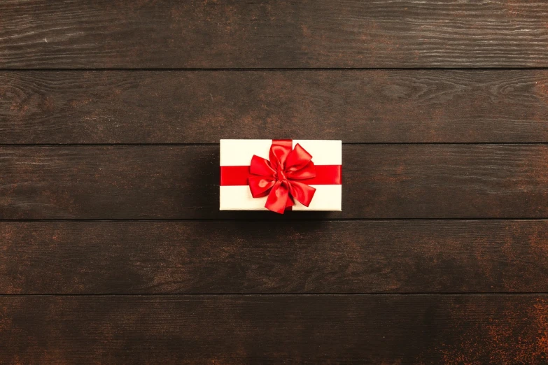 a white box with a red bow on a wooden surface, a stock photo, top - down photo, illuminated, packshot, decorated