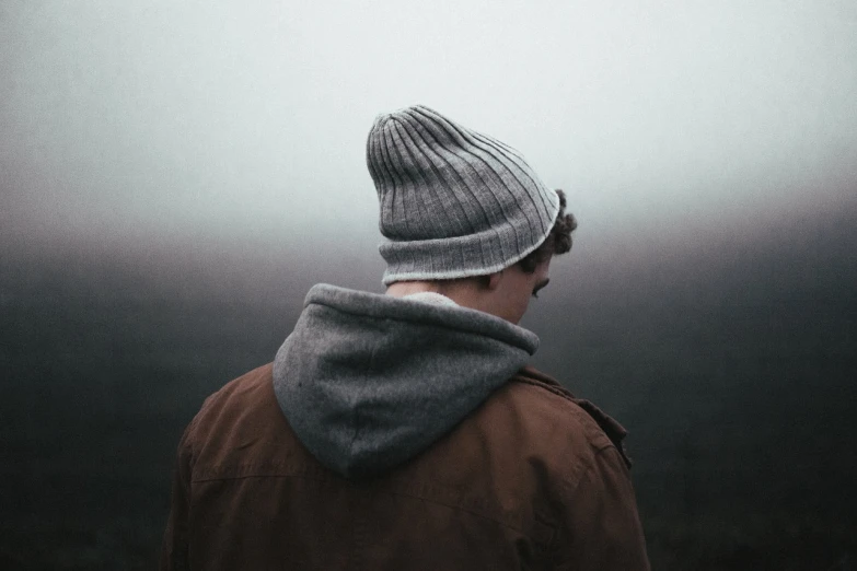 a close up of a person wearing a hat, by Karl Buesgen, unsplash, gray hoodie, with his back turned, gloomy and foggy atmosphere, short hair on top of his head