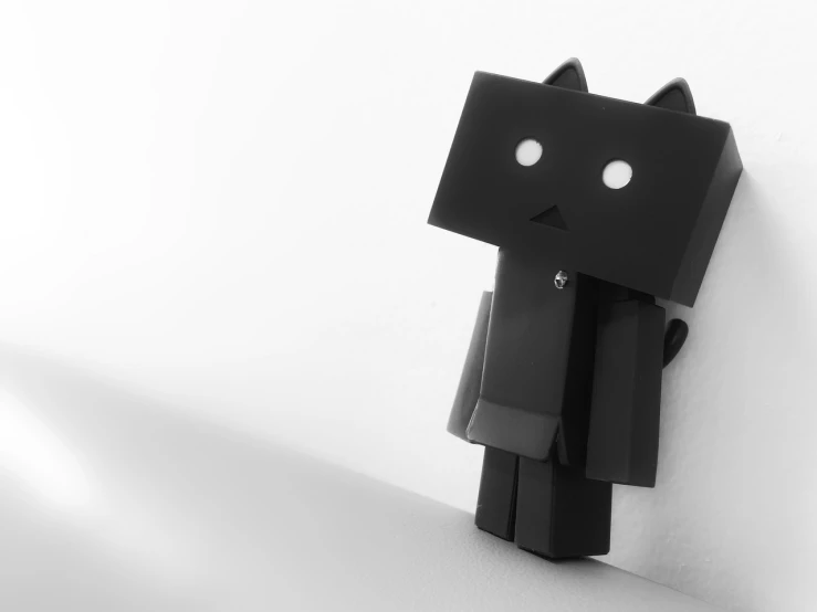 a black and white photo of a small robot, inspired by Jean Tabaud, tumblr, black cat, black 3 d cuboid device, male android, wall ]