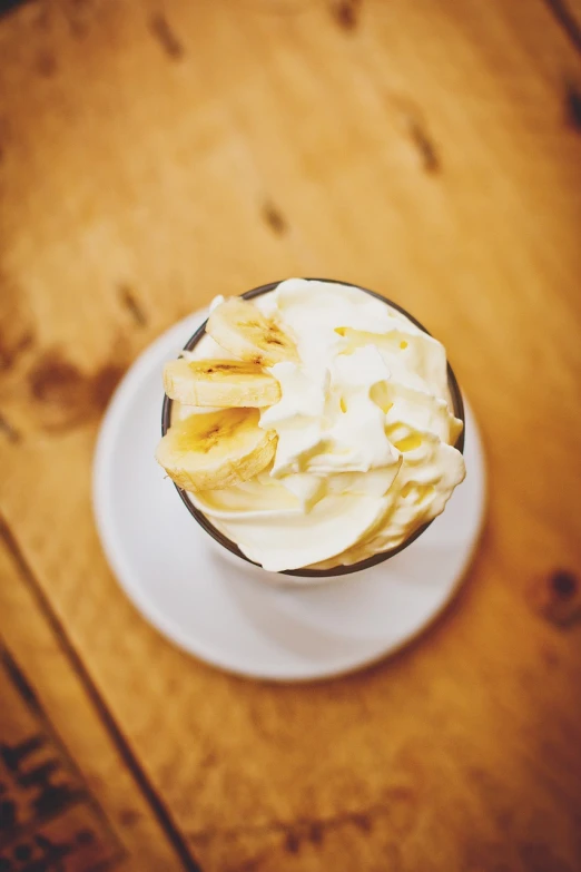 a cup of coffee sitting on top of a wooden table, a tilt shift photo, bananas, whipped cream on top, high detail product photo, viewed from below