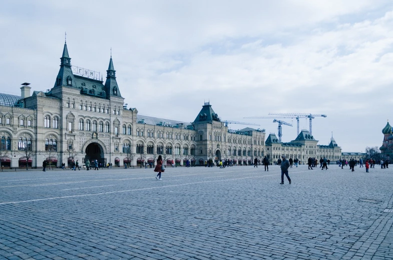 a group of people walking in front of a large building, a photo, inspired by Vasily Surikov, unsplash, socialist realism, city square, blue cobblestones, very wide wide shot, from inside the giant palace