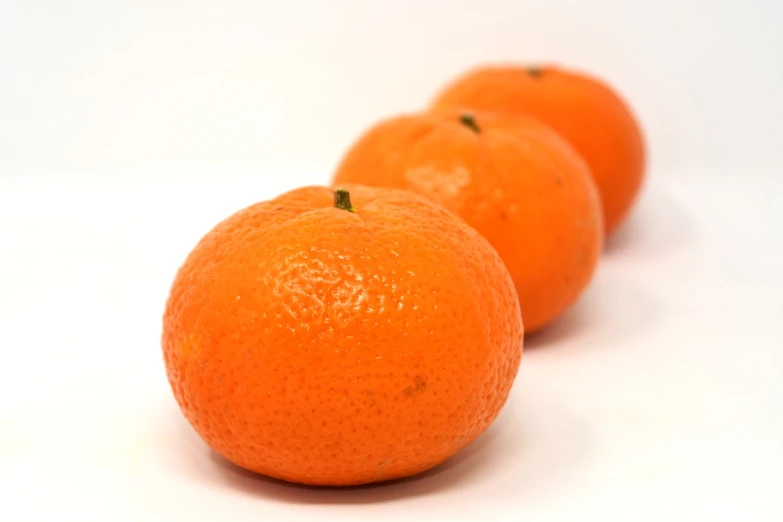 three oranges sitting next to each other on a white surface, mingei, very known photo