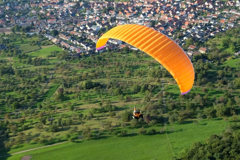 a person flying a parachute over a lush green field, a picture, by Karl Völker, orange roof, flying over a city, vivid colours. sharp focus. wow!, aero dynamic