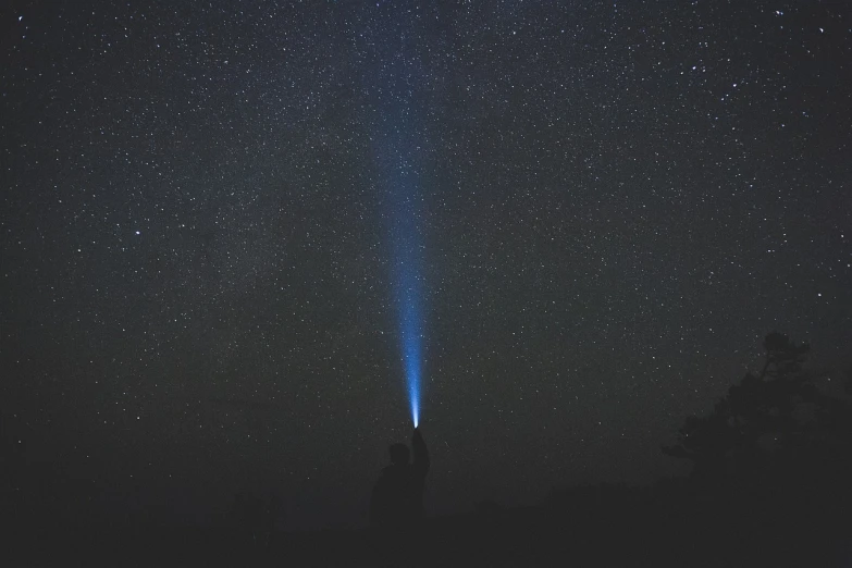 a person standing on top of a hill under a sky full of stars, a picture, by Adam Marczyński, light and space, blue v2 rocket in space, calm night. over shoulder shot, light cone, holy light halo