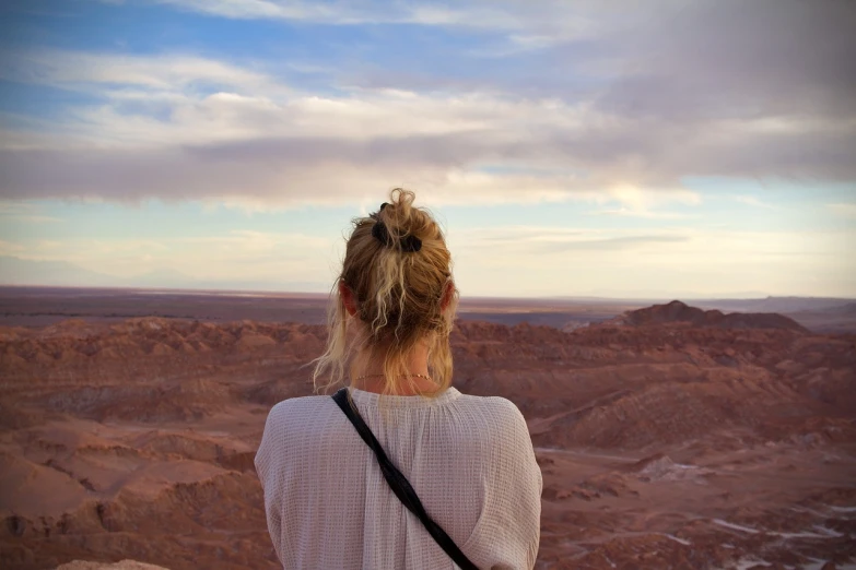 a woman looks out over a desert landscape, a picture, happening, mars vacation photo, beautiful lonely girl, long distance photo, looking across the shoulder