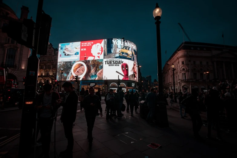 a crowd of people walking down a street at night, a picture, digital advertisements, in london, digital billboard in the middle, 2 0 2 2 photo