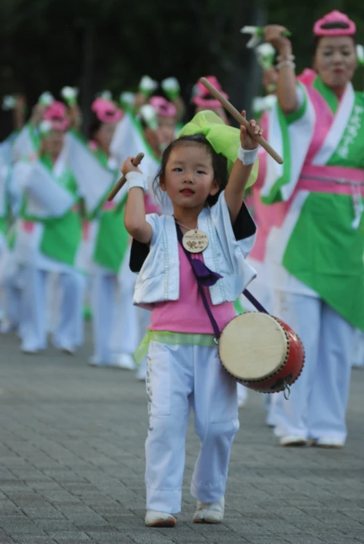 a little girl holding a drum in front of a group of people, inspired by Miao Fu, flickr, happening, pink white and green, triumphant pose, square, omina tachibana