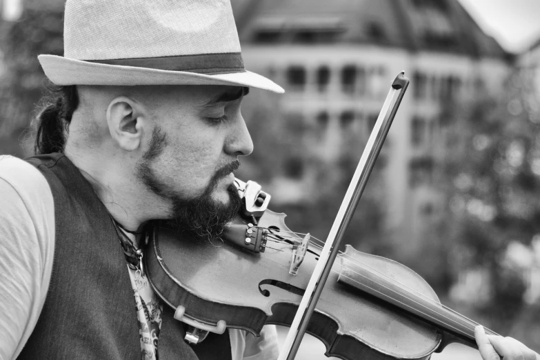 a man with a hat playing a violin, a black and white photo, inspired by Federico Zandomeneghi, pixabay contest winner, looking to the side off camera, in an urban setting, live performance, new mexico