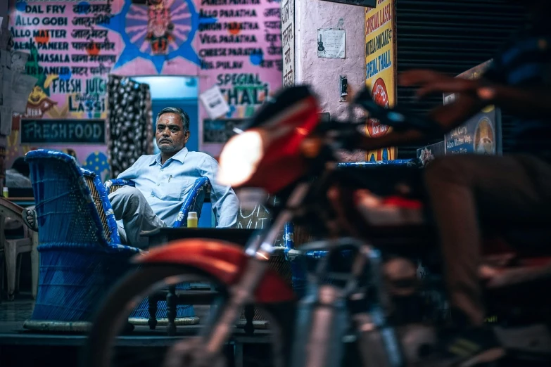 a man sitting in a chair next to a motorcycle, pexels contest winner, hyperrealism, neon shops, vijay jayant props, strong bokeh, movie still of a tired