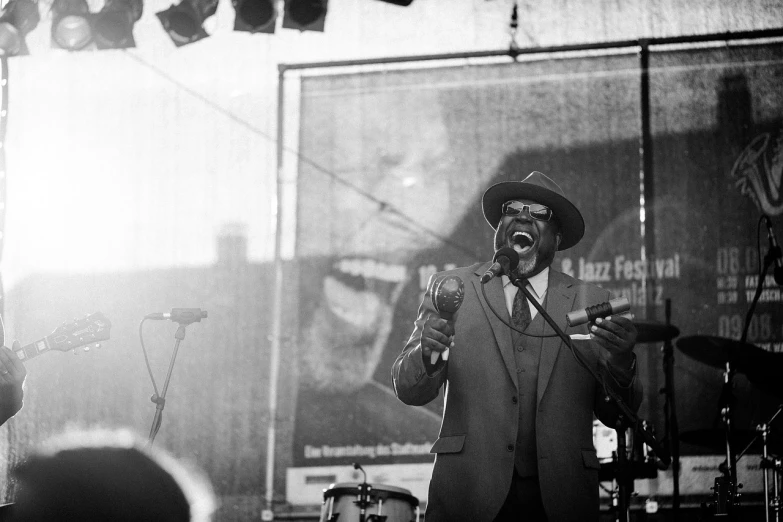 a man in a suit and hat singing into a microphone, a black and white photo, by Dan Frazier, funk art, shot on hasselblad, low sun, blues, instagram photo