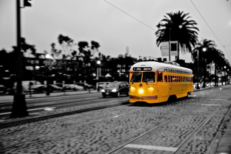 a yellow bus driving down a street next to palm trees, a tilt shift photo, by Chris Spollen, art photography, trams ) ) ), black and white and gold”, sf, phone wallpaper