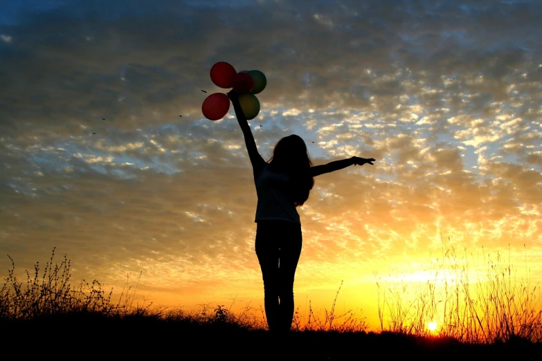 a woman holding a bunch of balloons at sunset, istockphoto, arms open, dlsr photo, with backlight