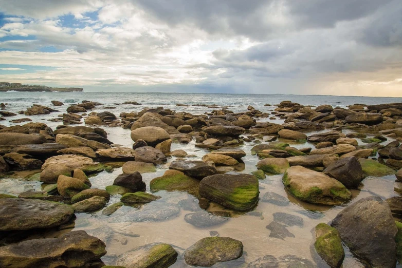 a group of rocks sitting on top of a sandy beach, sydney, today\'s featured photograph 4k, mossy rocks, brooding clouds'