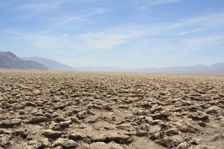a dirt field with mountains in the background, flickr, land art, cracked dry lake bed, it's californication, lumpy skin, rocky terrain