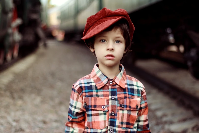 a young boy standing in front of a train, pexels, red ascot and a field cap, plaid shirt, frown fashion model, cute pout