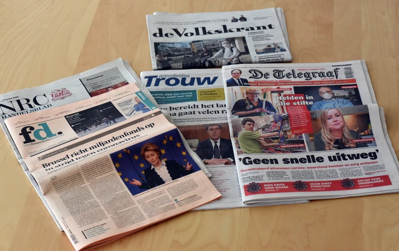 a pile of newspapers sitting on top of a wooden table, a picture, by Jacob Toorenvliet, private press, geert wilders, cornelia geppert, very very happy!, photo taken from above