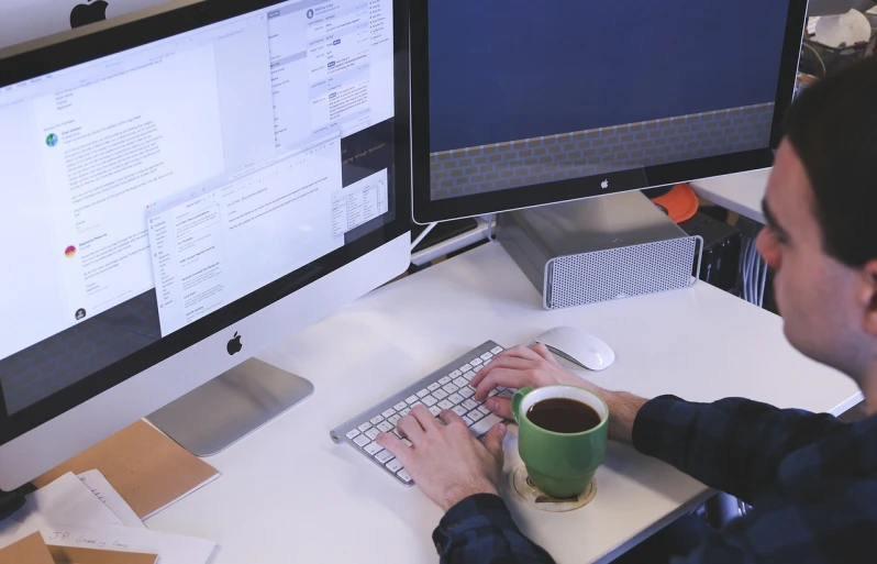 a man sitting at a desk typing on a keyboard, a computer rendering, by Romain brook, pexels, stacked computer screens, coffee, low quality photo, writing a letter