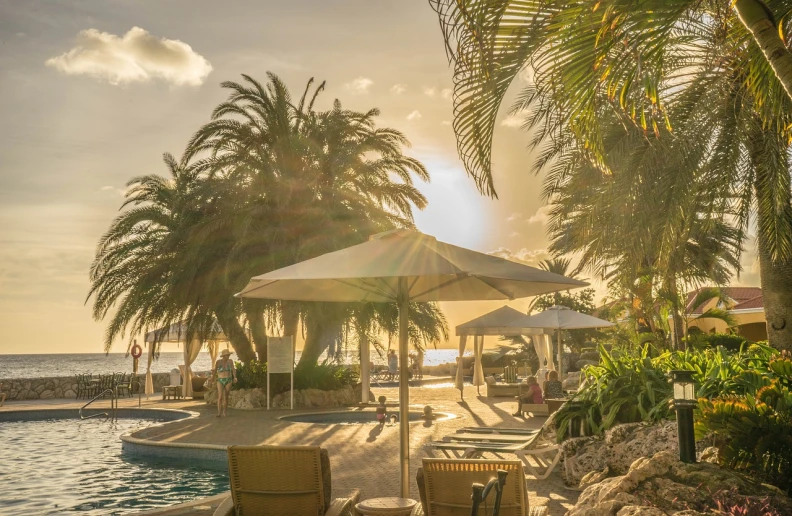 a couple of lawn chairs sitting next to a swimming pool, by Thomas Häfner, pexels, realism, palm trees on the beach, golden hour sun rays, aruba, hdr shot