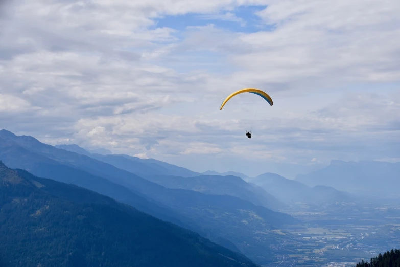 a person paragliding in the mountains on a cloudy day, a picture, figuration libre, bc, vacation photo, viewed from above, blue sky