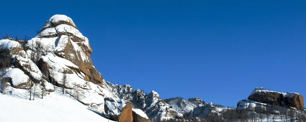 a man riding skis down a snow covered slope, inspired by Saitō Kiyoshi, flickr, rock formations, clear blue sky, banner, qiangshu