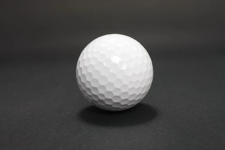 a white golf ball on a black surface, product photograph, hexagon, in front of a round, front facing