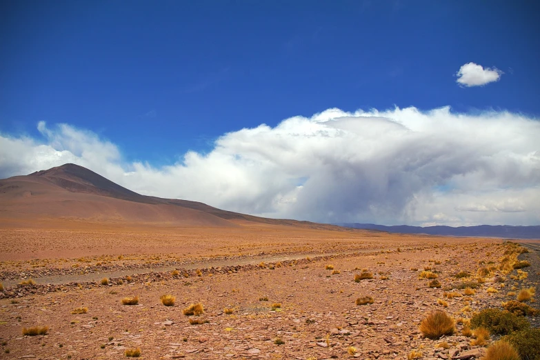 a dirt field with a mountain in the background, flickr, color field, andes, big cumulonimbus clouds, red desert, lê long