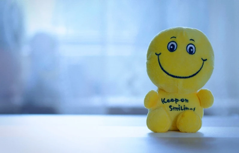 a yellow stuffed toy sitting on top of a table, a picture, pexels, focus on smile, motivational, edited, smiling kindly