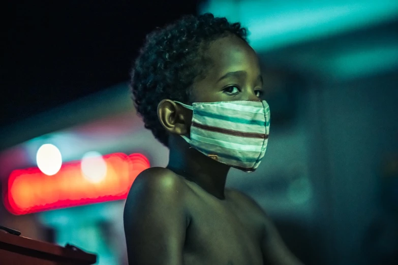 a close up of a child wearing a face mask, a picture, by João Artur da Silva, afrofuturism, photo taken at night, street life, the movie, dusty air