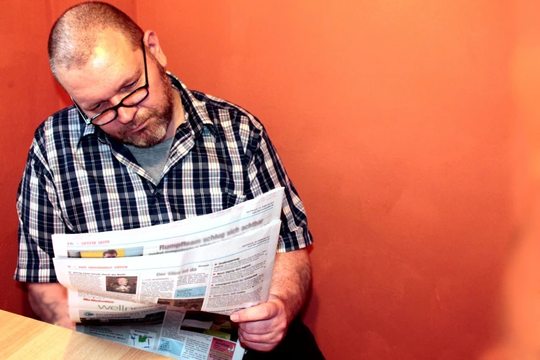 a man sitting at a table reading a newspaper, a photo, by Robin Guthrie, private press, ginger bearded man with glasses, blog-photo, profile photo, man in his 40s