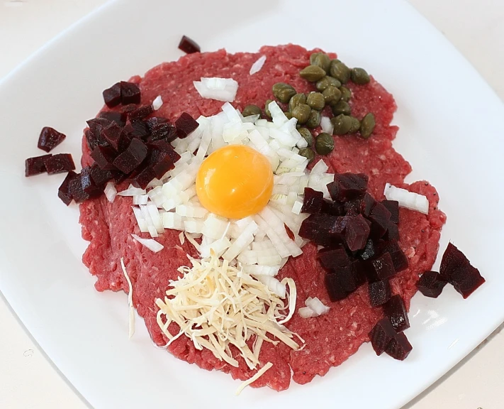 a white plate topped with meat and vegetables, a photo, inspired by Kalervo Palsa, renaissance, eggs, red meat shreds, raw, ground beef