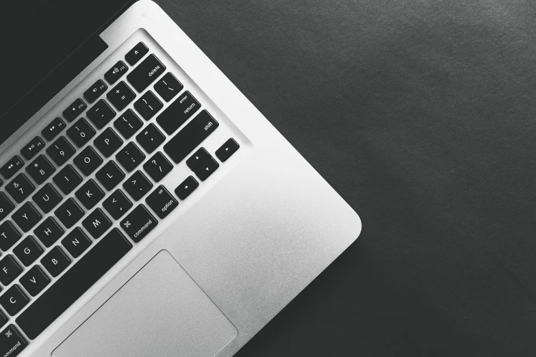 a laptop computer sitting on top of a table, a black and white photo, by Andrei Kolkoutine, pexels, solid background, high angle close up shot, silver, apple design