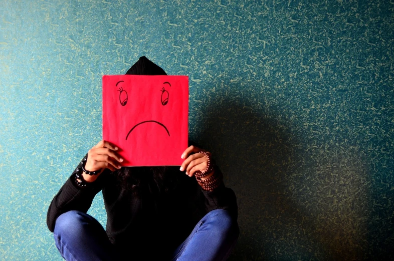 a person holding a piece of paper with a sad face drawn on it, by Matija Jama, pixabay, aestheticism, red face, sad colors, instagram picture, smiles in despair