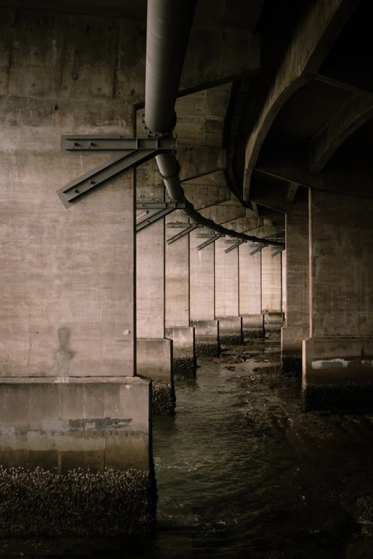 the underside of a bridge over a body of water, a portrait, unsplash contest winner, brutalism, drainpipes, [[empty warehouse]] background, river flowing through a wall, bleak lighting