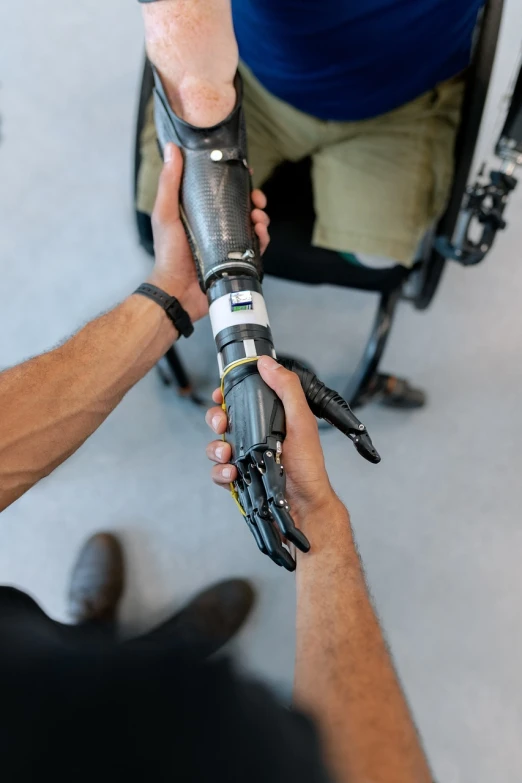 a man in a wheel chair holding a robotic arm, a picture, by Jakob Gauermann, unsplash, highly realistic hands, synthetic bio skin, 🦑 design, holding an activated lightsaber